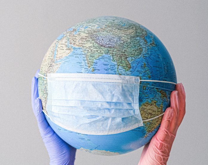 hands-with-latex-gloves-holding-a-globe-with-a-face-mask-4167544
